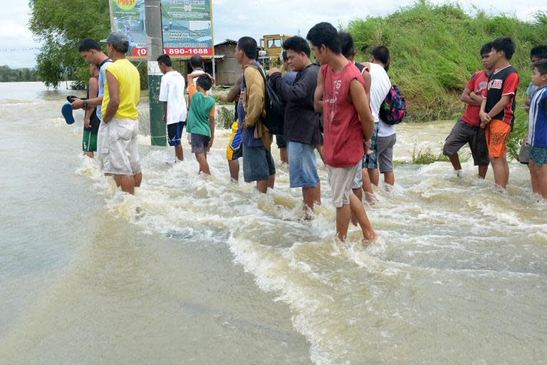 Stranded commuters stand in flood water on a road in northern Philippines on October 12, 2013