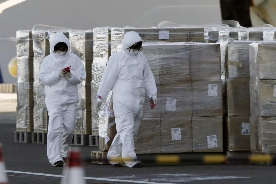 Officials in protective suits walk alongside supplies to be loaded on to the cruise ship Diamond Princess which is anchored at Yokohama Port in Yokohama, south of Tokyo, Thursday, Feb. 6, 2020. Health workers said 10 more people from the Diamond Princess were confirmed ill with the virus, in addition to 10 others who tested positive on Wednesday. They were dropped off as the ship docked and transferred to nearby hospitals for further test and treatment. (AP Photo/Eugene Hoshiko)