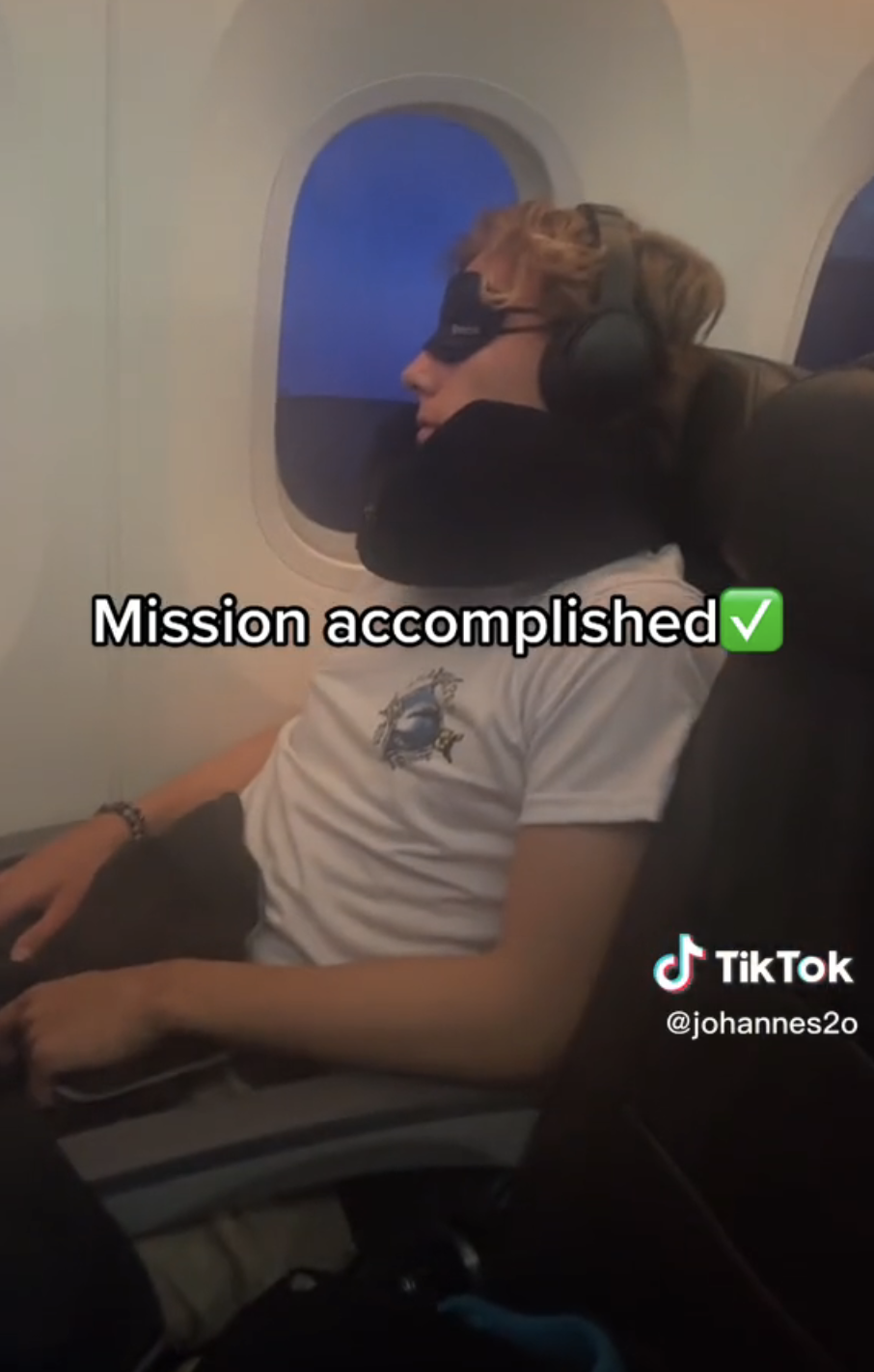 Man sitting on a plane wearing eye mask and neck pillow with caption "Mission accomplished" and check mark emoji