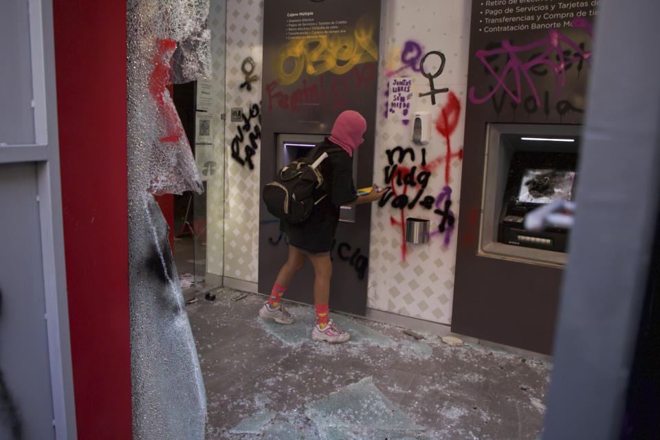 A woman sprays graffiti at a vandalized bank branch during march against gender-based violence, marking International Women's Day, in Mexico City, Wednesday, March 8, 2023. (AP Photo/Jessica Espinosa)