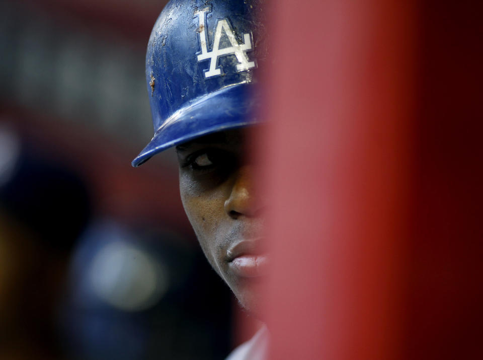 FILE - In this April 12, 2014 file photo, Los Angeles Dodgers' Yasiel Puig peers out from the dugout during the first inning of a baseball game against the Arizona Diamondbacks in Phoenix. Puig fled Cuba on a boat run by smugglers who allegedly made death threats against him and a boxer, according to court documents. The papers describe a dangerous odyssey of shady characters, unpaid debts and violence. (AP Photo/Ralph Freso, File)