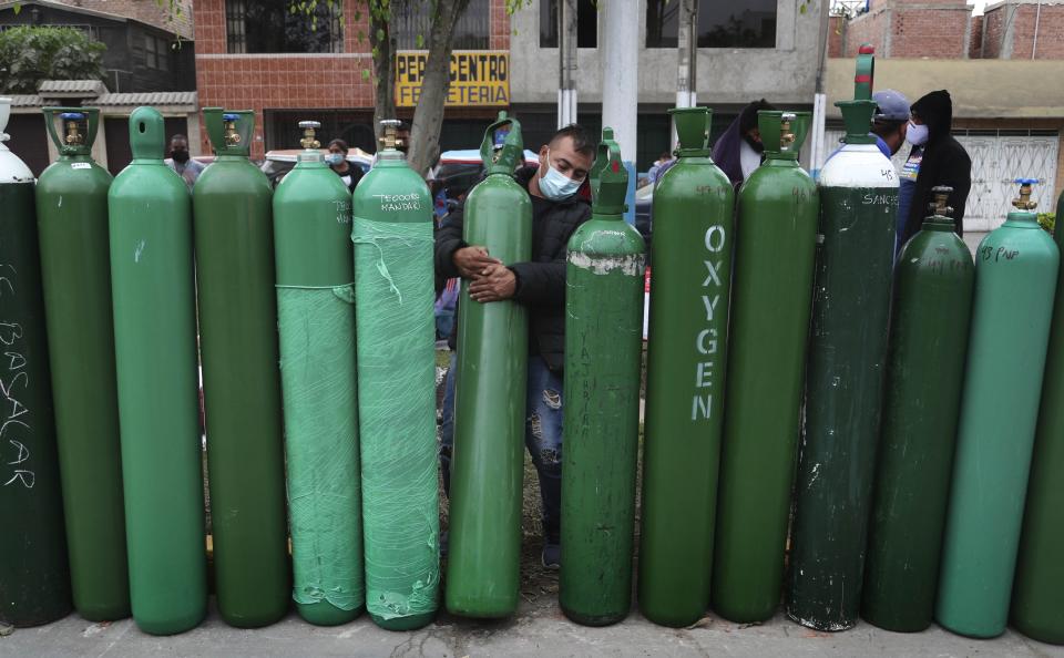 Edgar Barbaran exchanges a small, empty oxygen tank for this large one in a line of other people's tanks as he waits since the previous day for a refill shop to open in Callao, Peru, Monday, Jan. 25, 2021, amid the COVID-19 pandemic. Some people said they arrived to get in line on Sunday after the store closed in order to be first in line on Monday, while others missed out on Sunday's allotments of refills, approximately 80 tanks, and stayed to wait a second day. (AP Photo/Martin Mejia)