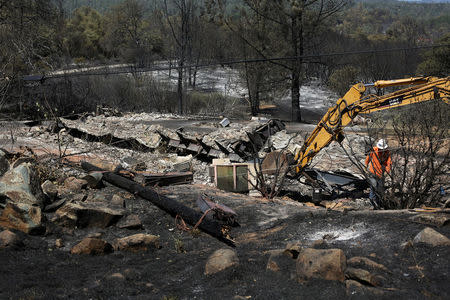 A crew member prepares to replace a downed power pole next to the remnants of a home burned by the Wall Fire near Oroville, California, July 10, 2017. REUTERS/David Ryder