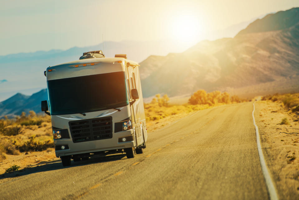 An RV drives along a rural road as the sun sets behind it.