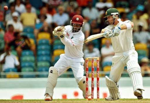 Australian cricket team captain Michael Clarke (R) plays a shot as West Indies wicketkeeper Carlton Baugh looks on during the third day of the first-of-three Test matches between Australia and West Indies at the Kensington Oval stadium in Bridgetown