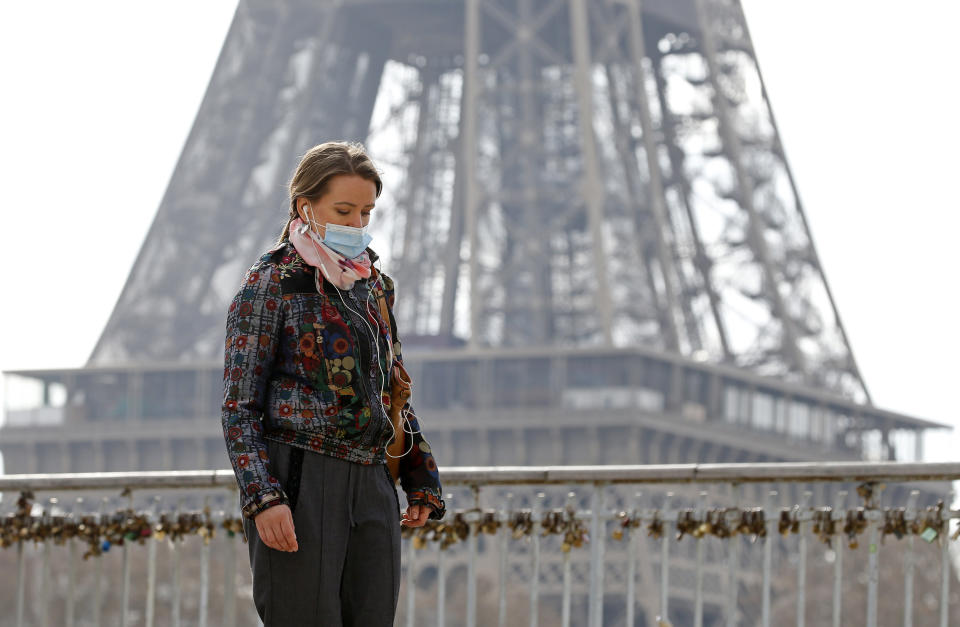 A woman is a mask in front of the Eiffel Tower in Paris. Source: Getty