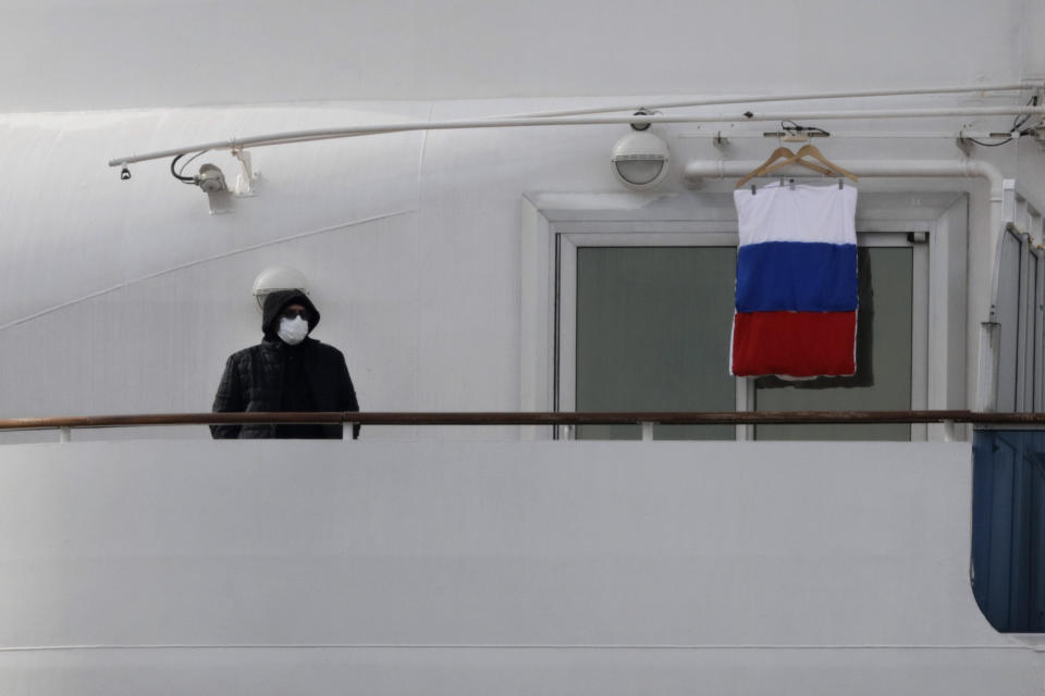 A quarantined passenger on the Diamond Princess cruise ship stands on the balcony of his cabin next to a Russian flag Saturday, Feb. 15, 2020, in Yokohama, near Tokyo. A viral outbreak that began in China has infected more than 67,000 people globally. The World Health Organization has named the illness COVID-19, referring to its origin late last year and the coronavirus that causes it. (AP Photo/Jae C. Hong)