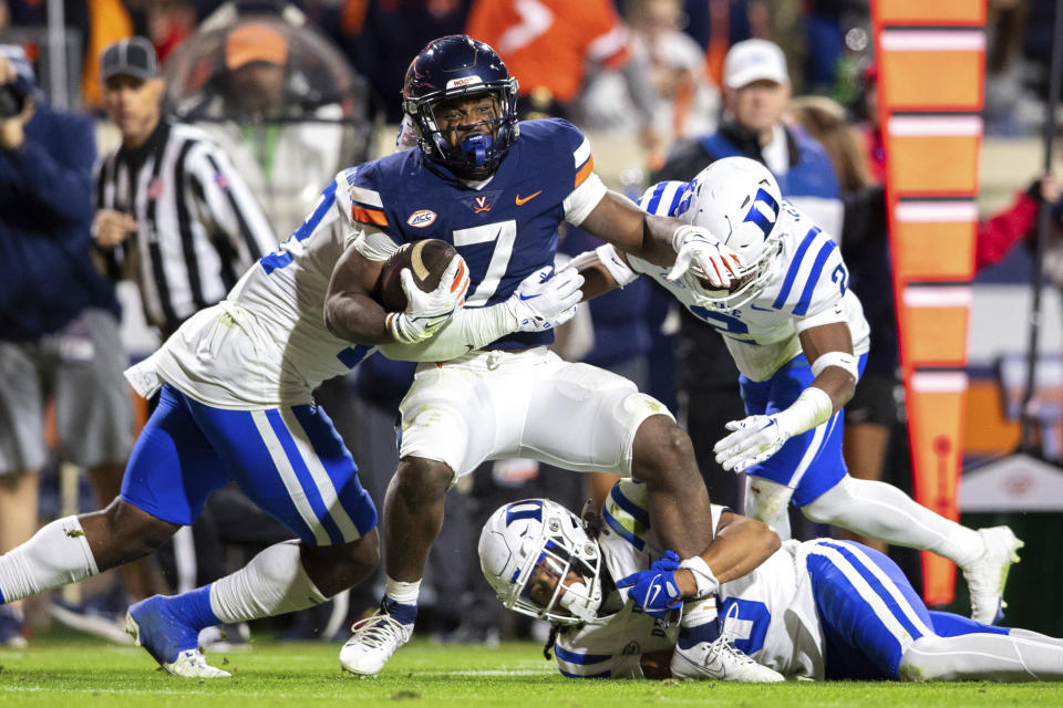 FILE - Virginia running back Mike Hollins (7) is tackled by Duke linebacker Tre Freeman, left, nose tackle Brandon Johnson, bottom, and safety Jaylen Stinson, right, during the second half of an NCAA college football game Saturday, Nov. 18, 2023, in Charlottesville, Va. Hollins, who survived a shooting that left three of his teammates dead and returned to the Cavaliers less than a year later, is one of three recipients of college football’s Comeback Player of the Year Award, announced Monday, Dec. 18. (AP Photo/Mike Caudill, File)