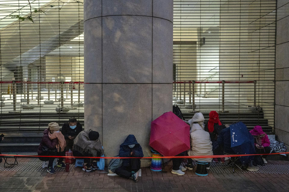 People wait behind a police line set up outside West Kowloon Magistrates' Courts, where Jimmy Lai's trial is scheduled to open, in Hong Kong, Monday, Dec. 18, 2023. (AP Photo/Vernon Yuen)