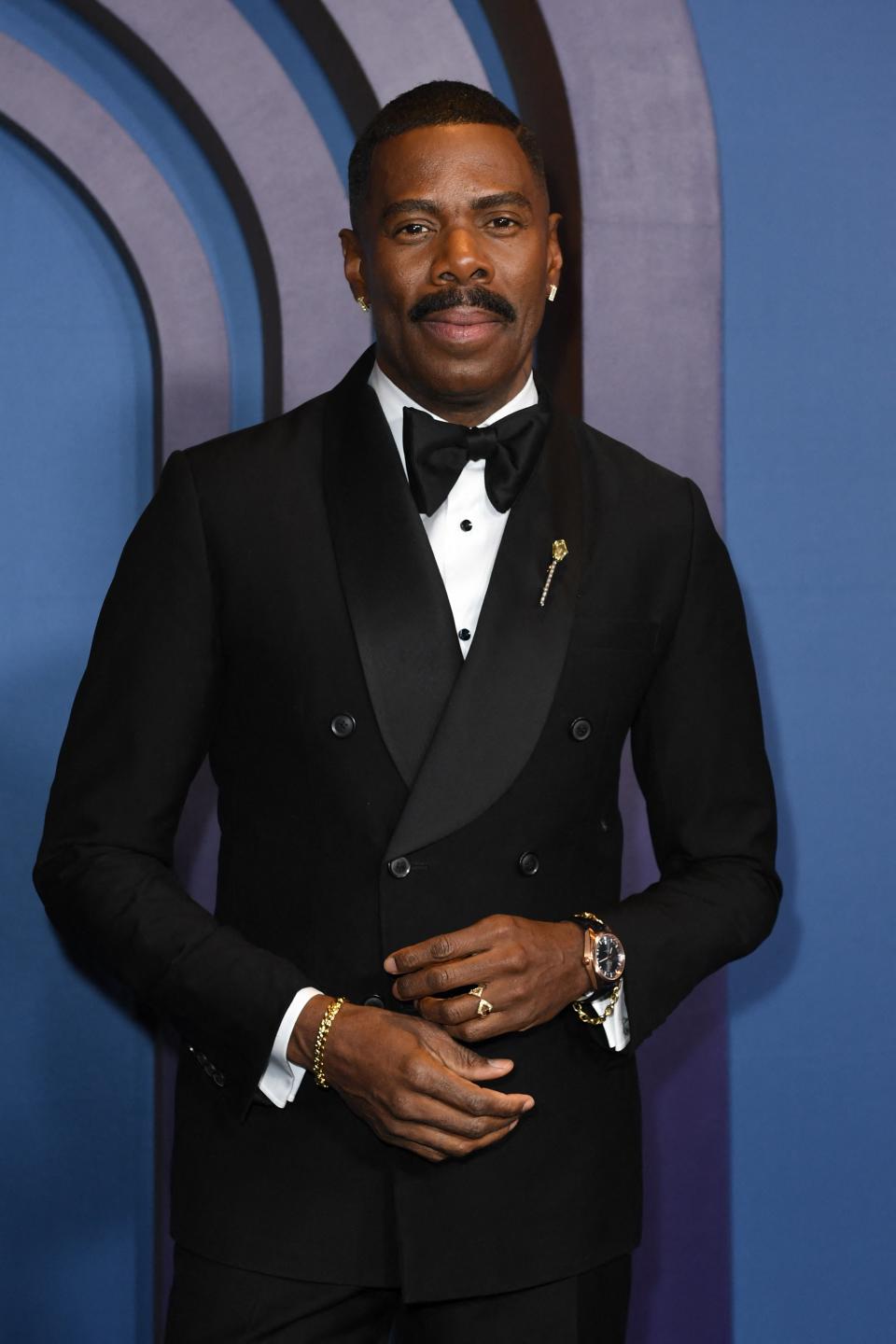 Colman Domingo in a tuxedo with a bow tie and small pin on his lapel, posing at an event