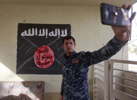 A member of the federal police forces takes a selfie in front of a defaced black flag commonly used by Islamic State militants, during a battle with Islamic State militants, in the Wahda district of eastern Mosul, Iraq, January 10, 2017. REUTERS/Alaa Al-Marjani