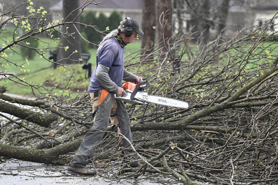 A worker cut up downed tress lying across the road following severe storms that passed through Prospect, Ky., Tuesday, April 2, 2024. (AP Photo/Timothy D. Easley)