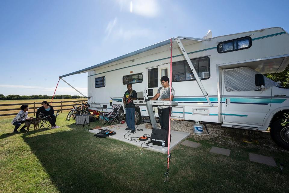 Roland and Clement Kemokai play music as Christine and Ben watch outside their trailer home in Granger. The Kemokai family makes their living in music and children's party entertainment. After losing their apartment and hotel, they moved into an RV.