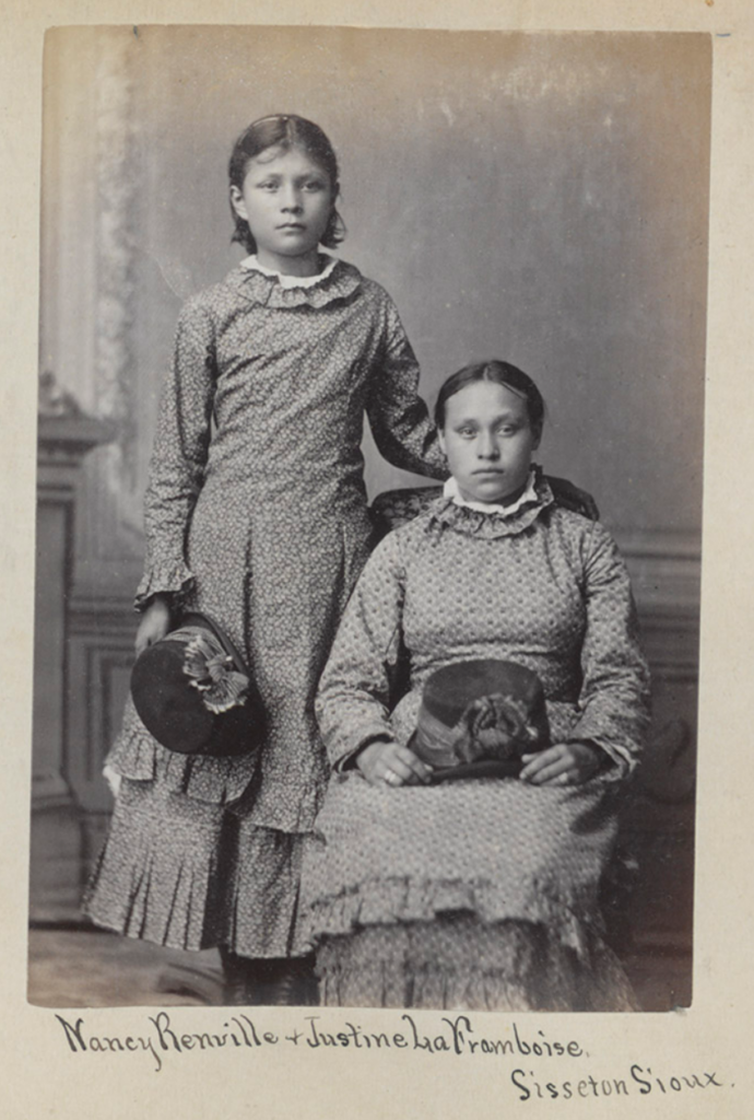 Nancy Renville and Justine La Framboise (left to right) of Sisseton Wahpeton Oyate pose for a photo at the Carlisle Indian Industrial School in Pennsylvania. Both wear school-issued print dresses.