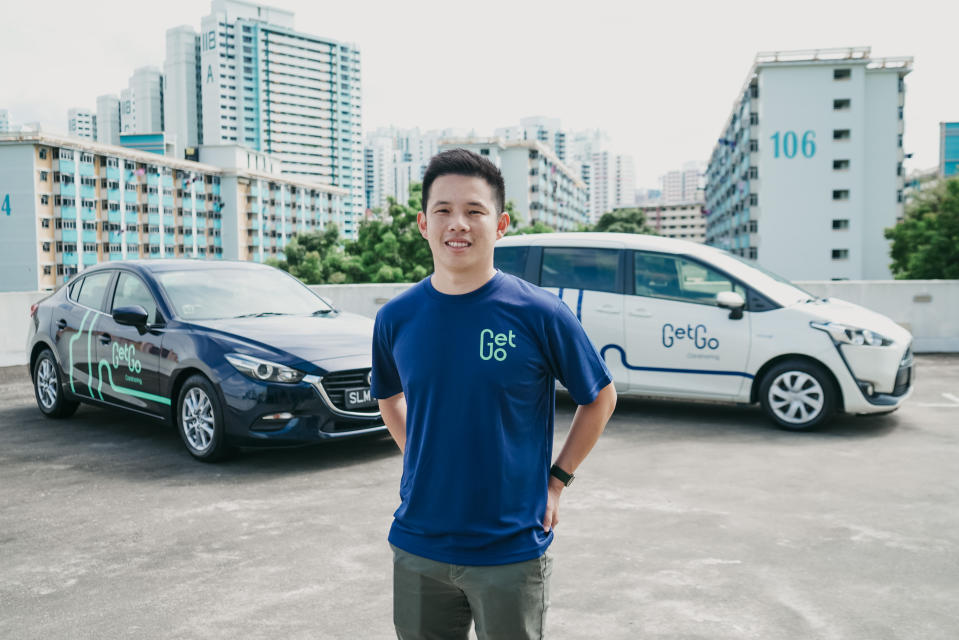 Toh Ting Feng, co-founder and CEO of car-sharing platform GetGo, posing with GetGo cars and HDB flats in the background.