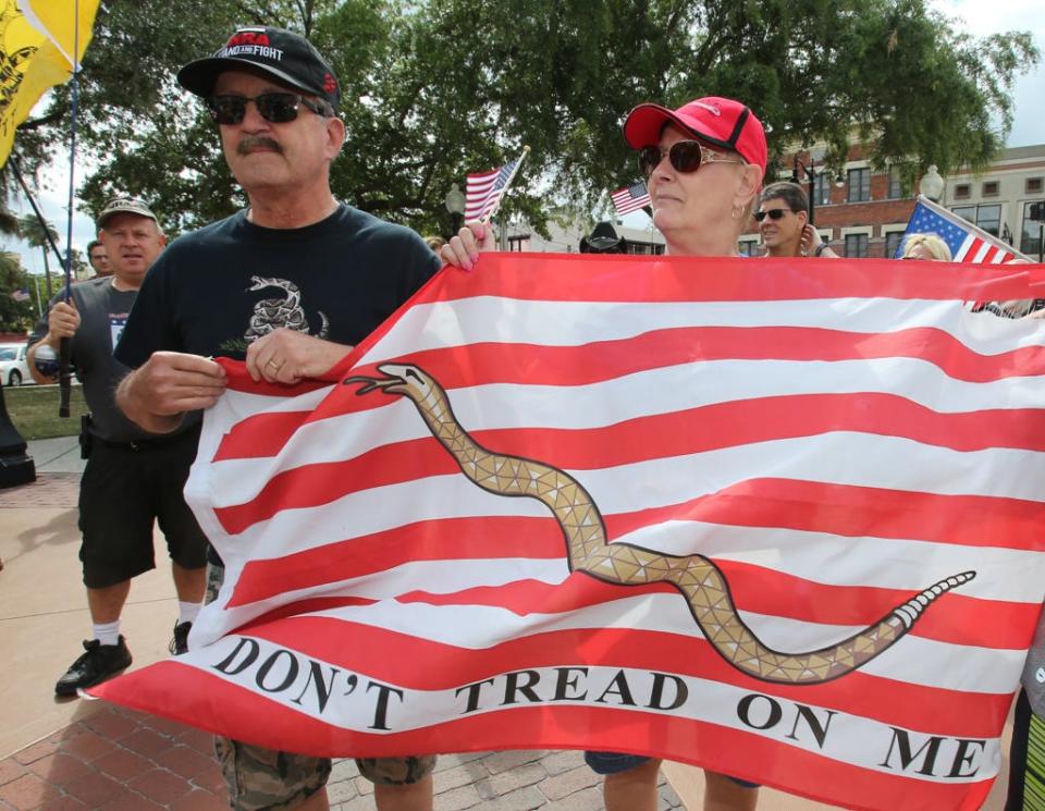 Jim and Nancy Dean of Summerfield hold a Navy Jack flag as they pause with other people to say The Pledge Of Allegiance and pray on the Ocala Downtown Square during the Open Carry March from the downtown parking garage to Tuscawilla Park in Ocala, Fla. on Saturday, April 7, 2018. Dozens of people from the Region 5 Florida Carry and the Florida Firearms Coalition marched peacefully to the Ocala park on Saturday. [Bruce Ackerman/Ocala Star-Banner] 2018.