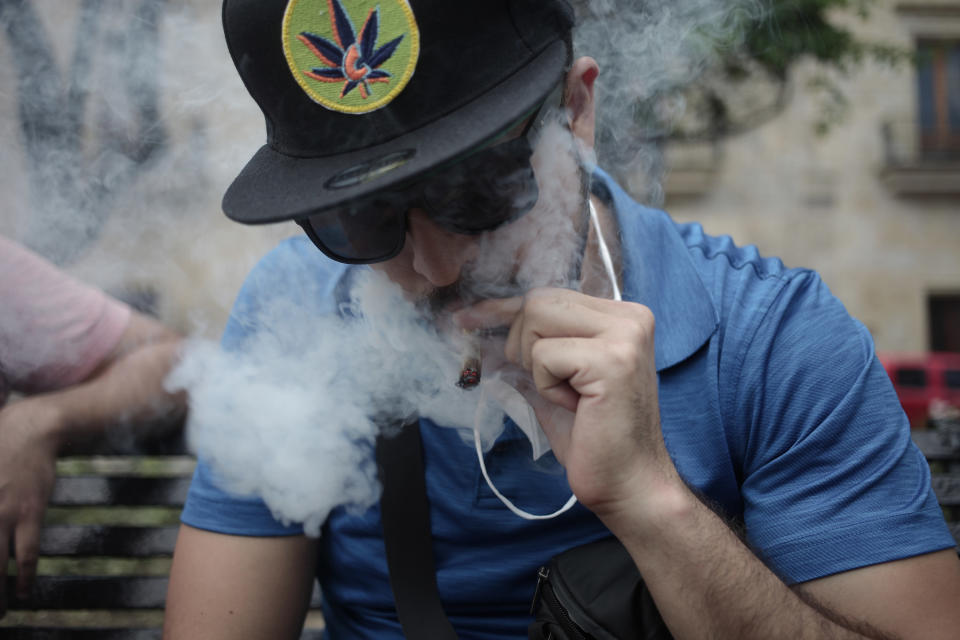 A guy smoking a joint wearing a marijuana hat and dark sunglasses