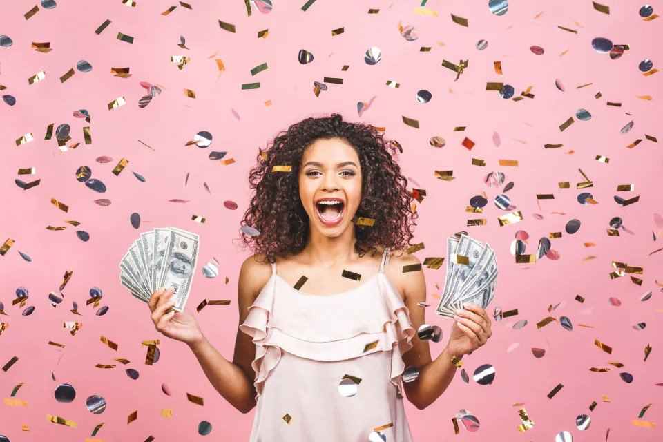 Happy young woman holding dollar currency satisfied isolated over pink background with confetti.