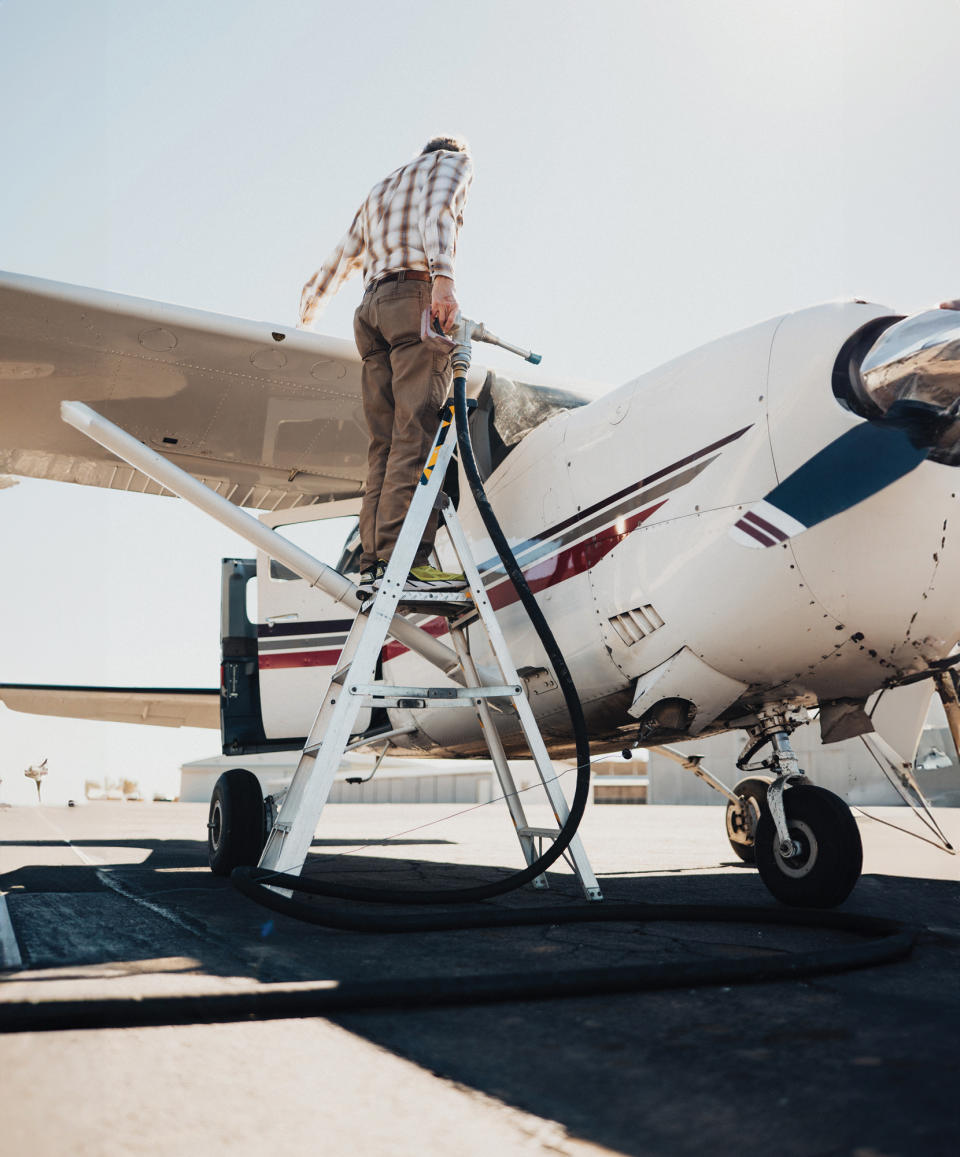 A man in a flannel putting fuel into his small Cessna plane.