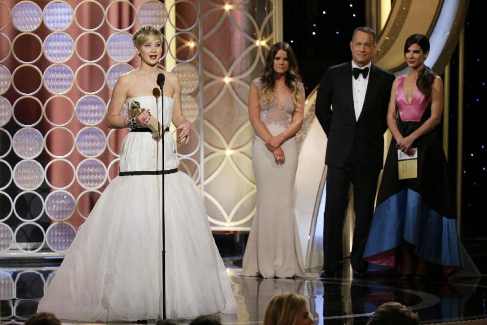 This image released by NBC shows Jennifer Lawrence, left, accepting the award for best supporting actress in a motion picture for her role in "American Hustle," as presenters Sandra Bullock, right, and Tom Hanks, second right, look on during the 71st annual Golden Globe Awards at the Beverly Hilton Hotel on Sunday, Jan. 12, 2014, in Beverly Hills, Calif. (AP Photo/NBC, Paul Drinkwater)