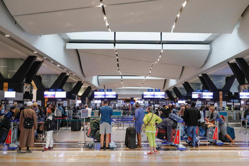 Travellers queue at a check-in counter at an airport.