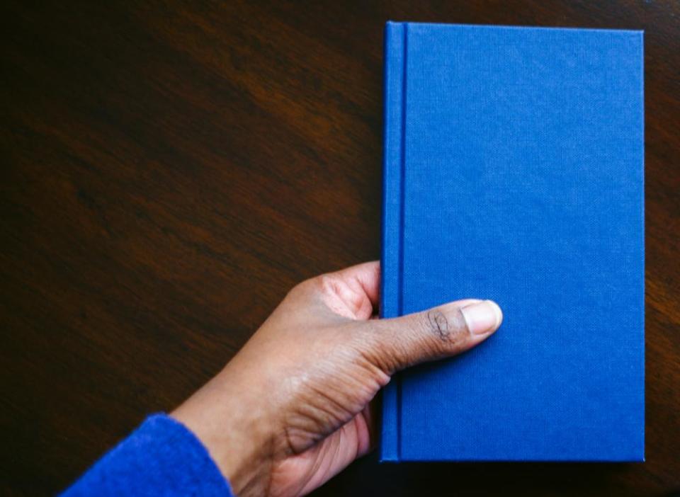 High angle view of woman’s hand picking up book from table