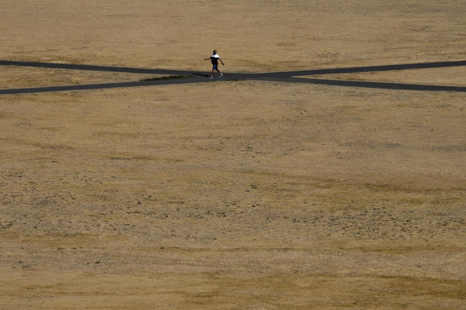 FILE - A man walks along a road through dry and sun burnt grass in Greenwich Park in London, Aug. 9, 2022. Ten years ago scientists warned the world about how climate change would amplify extreme weather disasters. There are now deadly floods, oppressive heat waves, killer storms, devastating droughts and what scientists call unprecedented extremes as predicted in 2012. (AP Photo/Frank Augstein, File)