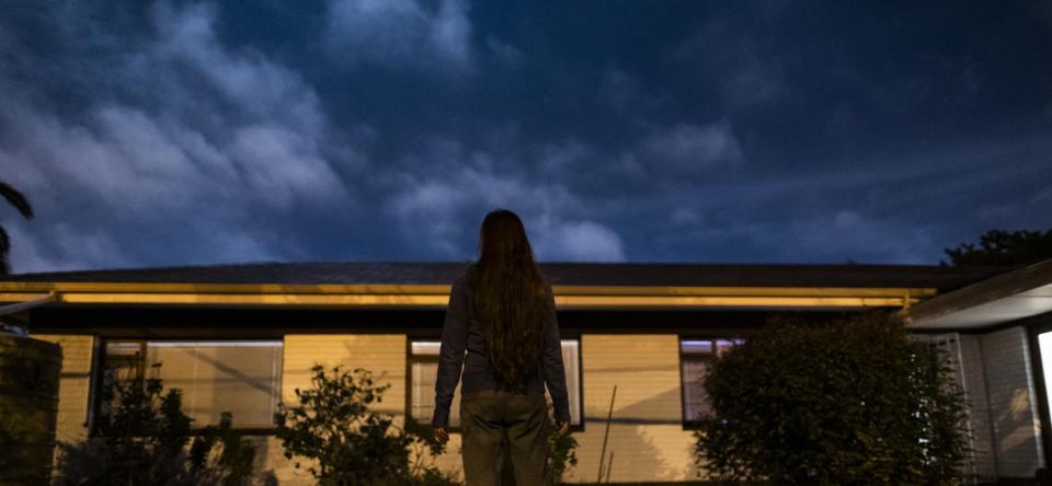 Young woman standing in front yard looking up to the moonlit night sky