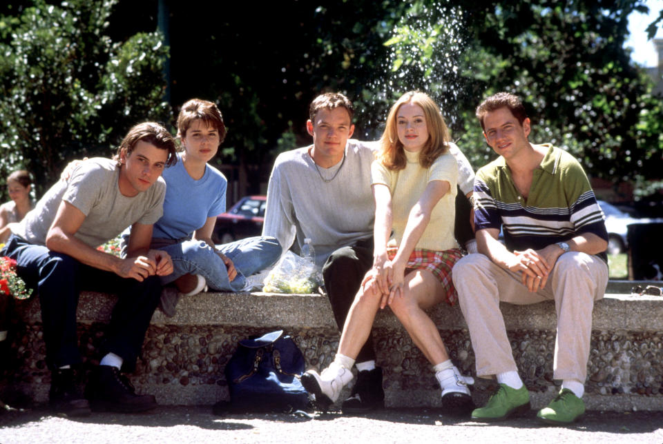 Five individuals sitting on a ledge outdoors, relaxed postures, casual attire