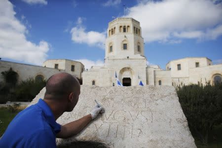 Shmulik Freireich, a worker for Israel Antiquities Authority (IAA), demonstrates the cleaning of an ancient Latin inscription engraved on a stone, displayed for the media outside Rockefeller Archaeological Museum in Jerusalem October 21, 2014. REUTERS/Ronen Zvulun