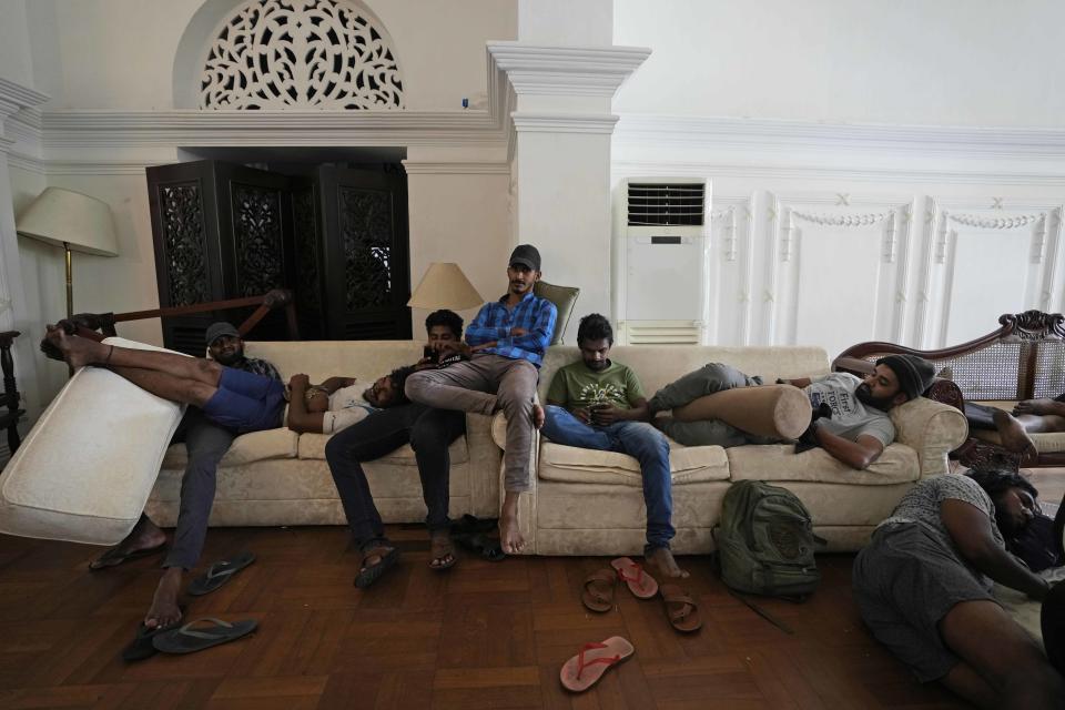 Protesters rest on sofas in the living hall of prime minister's official residence a day after vandalising it in Colombo, Sri Lanka, Sunday, July 10, 2022. Sri Lanka’s president and prime minister agreed to resign Saturday after the country’s most chaotic day in months of political turmoil, with protesters storming both officials’ homes and setting fire to one of the buildings in a rage over the nation's severe economic crisis. (AP Photo/Eranga Jayawardena)