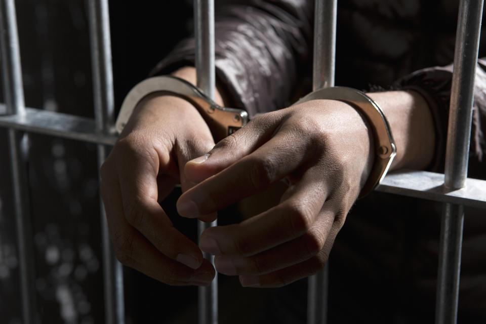 Person's hands in handcuffs gripping prison bars, representing an arrest or imprisonment