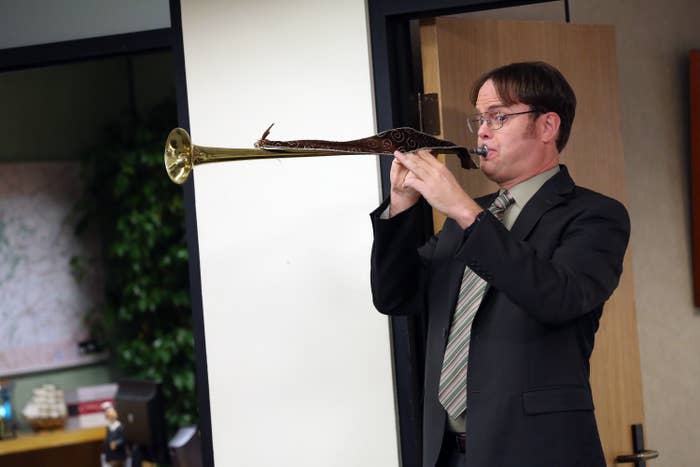 Actor in character playing a long brass instrument in an office setting