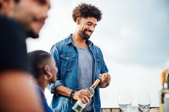 A man opening a bottle of wine to pour at an outdoor table with friends.