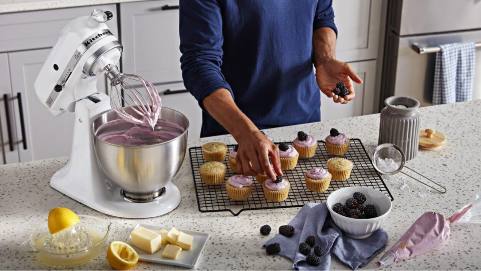 Someone decorating cupcakes with a KitchenAid stand mixer filled with frosting next to them