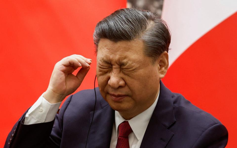 Xi Jinping grimaces and appears to adjust his earpiece during a signing ceremony at the Great Hall of the People