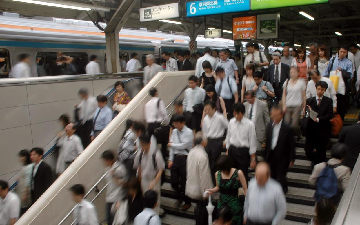 Commuters get out of a train at a railway station in Tokyo  - AP