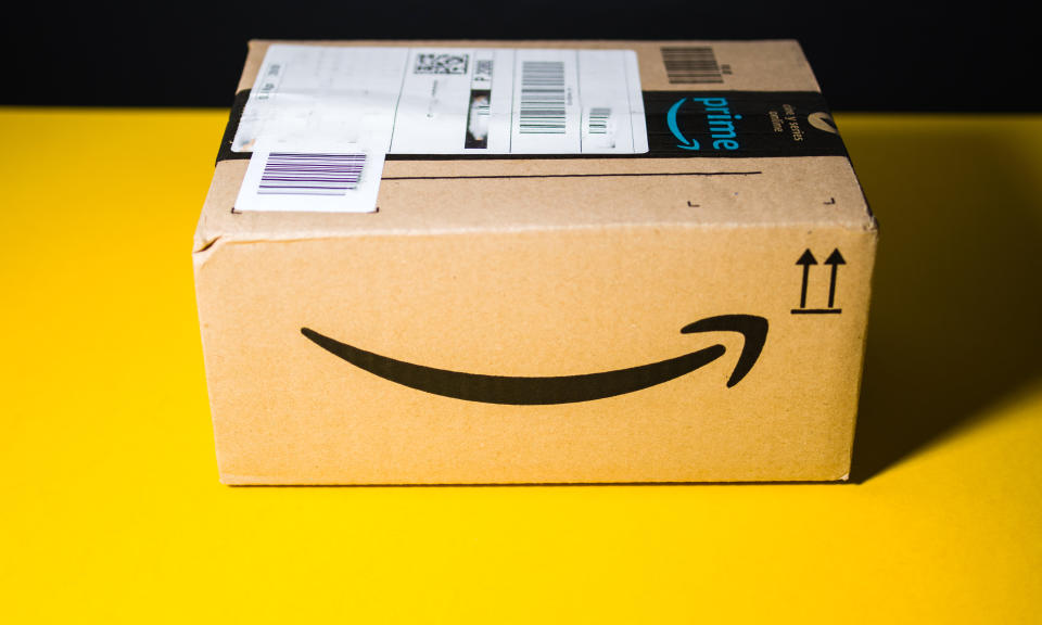 PARIS, FRANCE - SEP 28, 2018: Small Amazon parcel cardboard box against yellow background smile logo. Amazon Prime is the online paid subscription service offered by Amazon.com web-commerce site