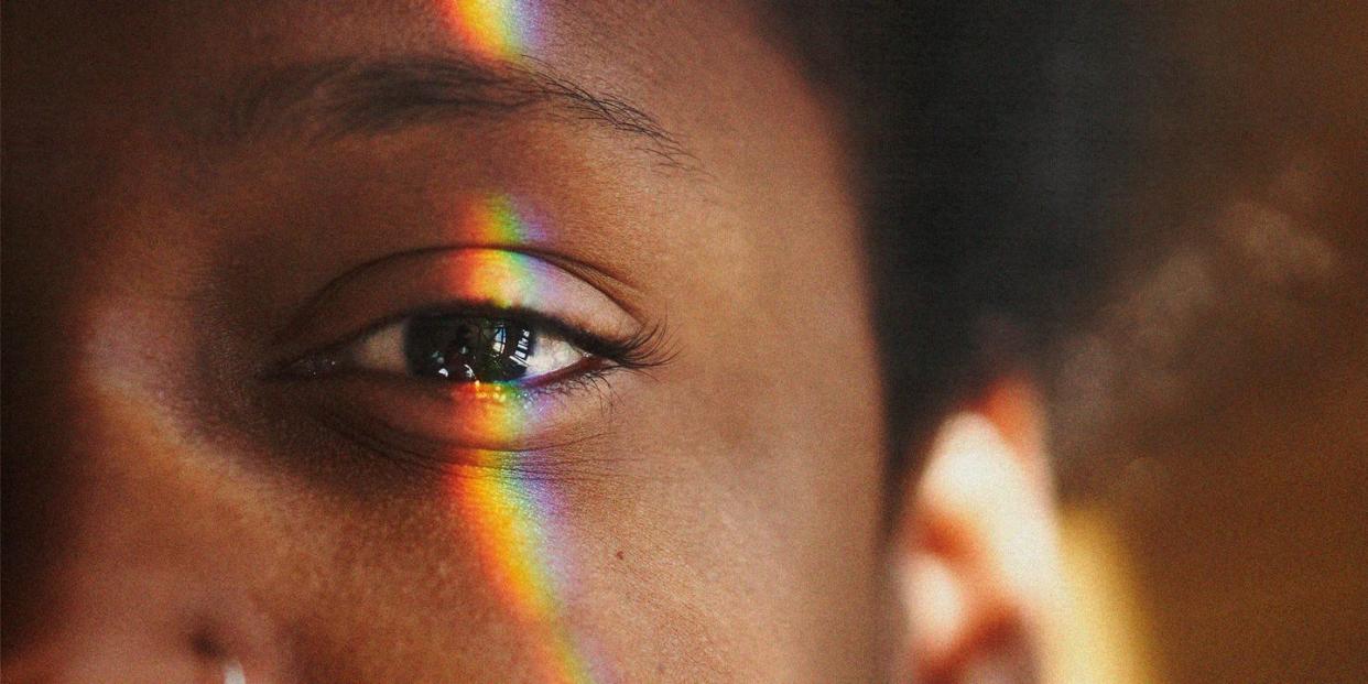 half of a black womans face with a rainbow light reflection over her eye