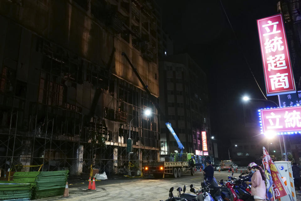 A woman stands across the street from the burnt building in Kaohsiung in southern Taiwan on Thursday, Oct. 14, 2021. Officials say at least 46 people were killed and over 40 injured after a fire broke out in a decades-old mixed commercial and residential building in the Taiwanese port city of Kaohsiunging. Neighborhood residents say the 13-story building was home to many poor, elderly and disabled people and it wasn’t clear how many of the 120 units were occupied. (AP Photo/Huizhong Wu)