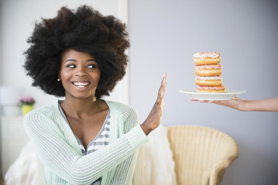 A woman smiles while playfully refusing a plate with a stack of donuts held out to her