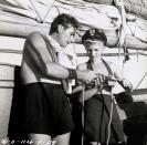 <p>Errol Flynn and Rita Hayworth match one another in high-waisted black shorts. The actress pairs hers with a black halter bikini top and a sailing cap, as Flynn shows her a sailing knot. </p>