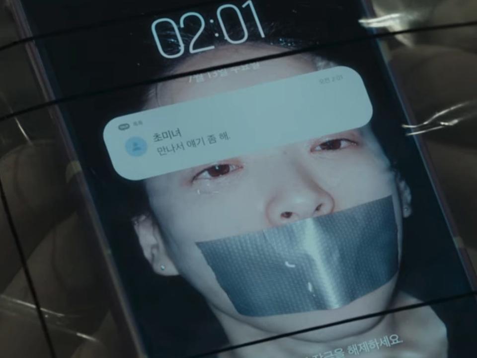 a notification on na-mi's cell phone in unlocked from her friend, saved in her contacts as "drop dead gorgeous." the text asks for them to meet up and talk. the phone's background is an image of na-mi in a bathtub, duct tape over her mouth