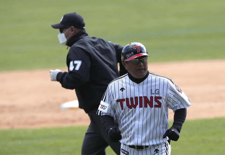 A letters reading "Corona 19 Out" is seen on the helmet of LG Twins baseball team's coach Kim Ho as third base umpire Choi Young-joo, left, wearing a mask and gloves as a precaution against the new coronavirus runs during the pre-season baseball game between Doosan Bears and LG Twins in Seoul, South Korea, Tuesday, April 21, 2020. South Korea's professional baseball league has decided to begin its new season on May 5, initially without fans, following a postponement over the coronavirus. (AP Photo/Lee Jin-man)