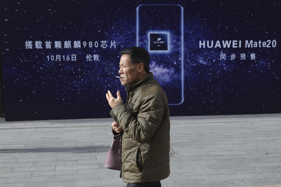 A man smokes as he pass by an advertisement for Huawei products in Beijing Monday, Jan. 7, 2019. Huawei Technologies Ltd. unveiled a processor chip Monday for data centers and cloud computing in a bid by the biggest global maker of telecom equipment to expand into new markets despite Western warnings the company might be a security risk. (AP Photo/Ng Han Guan)