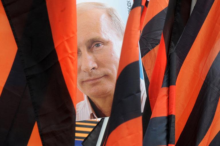 A protesters holds a portrait of Russian President Vladimir Putin behind flags of the ribbon of Saint George during a May Day rally in Saint Petersburg on May 1, 2015