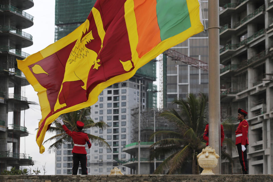 In this July 24, 2019, photo, a Sri Lankan army lowers the national flag at the landmark Galle Face, as new foreign investment sites stand in the background in Colombo, Sri Lanka. Shocks from deadly suicide bombings on Easter Day in Sri Lanka are reverberating throughout its economy in the worst crisis since the South Asian island nation’s civil war ended in 2009. The blasts have devastated Sri Lanka’s vital tourism industry, source of jobs for many, and hindering foreign investment. (AP Photo/Eranga Jayawardena)