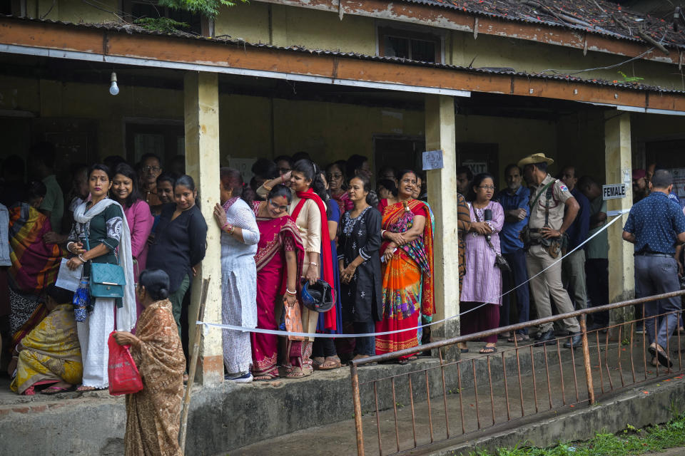 A security person stands guard as voters stand in queue to cast their votes in a polling station during the third phase of general election in Guwahati, India, Tuesday, May 7, 2024. (AP Photo/Anupam Nath)