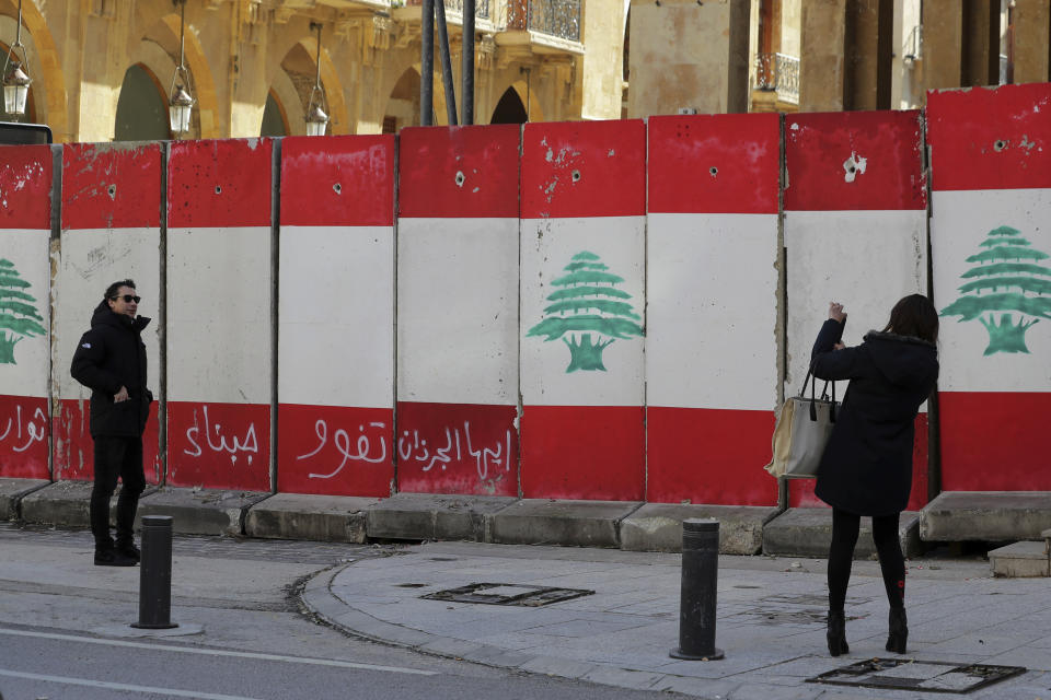 A man poses for a picture in front of a concrete wall installed by authorities to blocks a road leading to the parliament building, in Beirut, Lebanon, Friday, Jan. 24, 2020. As cement barricades come up across the capital, blocking the path to major government buildings, Lebanese protesters vowed to continue taking to the street on the 100-day anniversary of the anti-government protests. (AP Photo/Hassan Ammar)