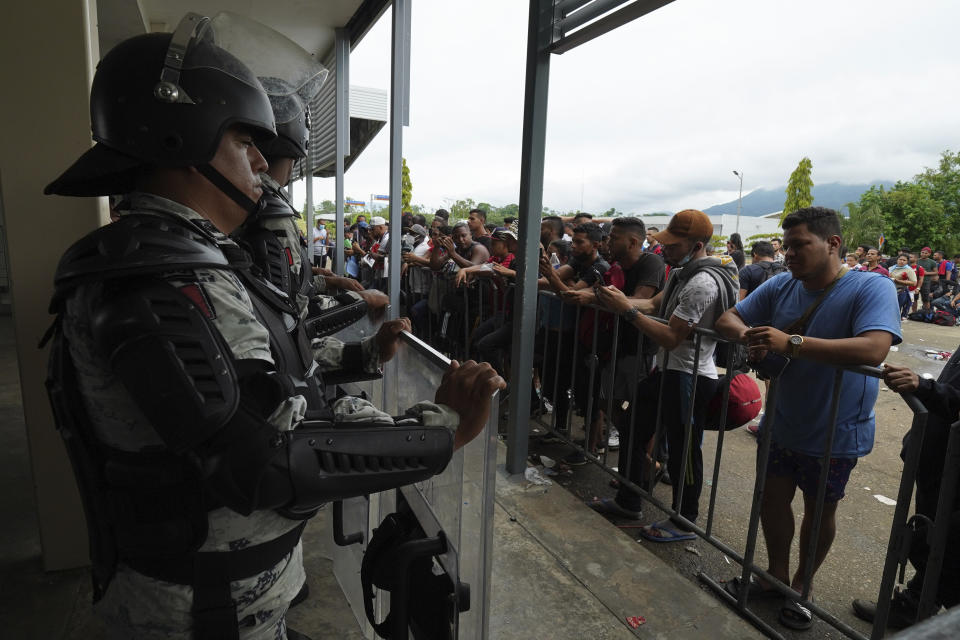 Migrants gather outside the Border Transit Comprehensive Care Center, guarded by security forces, to ask for legal documents that allow them to travel through Mexico, on the outskirts of Huixtla, Chiapas state, Mexico, Friday, June 10, 2022. The group left Tapachula this Monday, tired of waiting to normalize their status in a region with little work, with the ultimate goal of reaching the US. (AP Photo/Marco Ugarte)